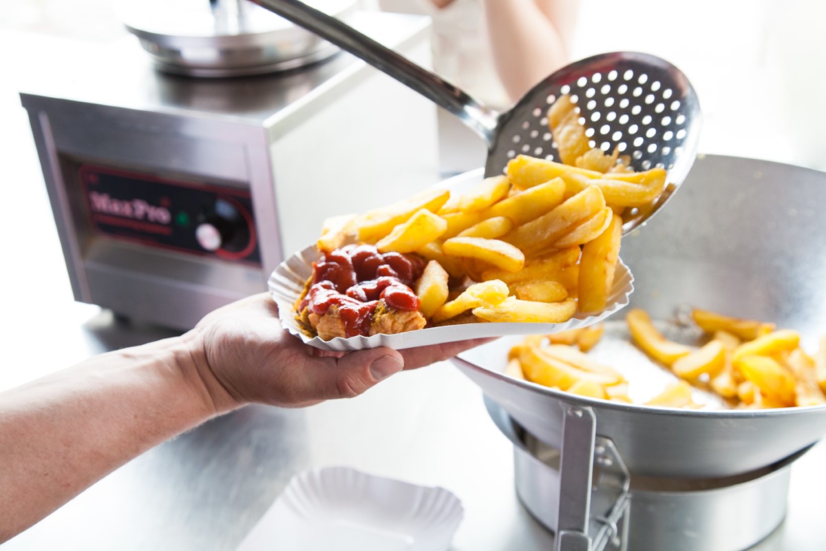 Witty's currywurst and fries are filled onto a white cardboard tray with a large ladle