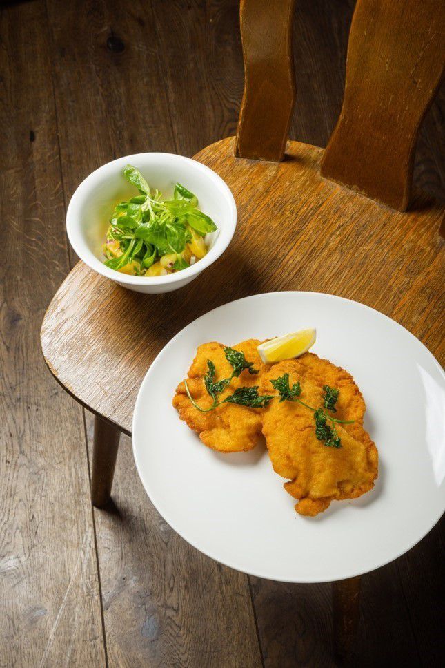 Wiener Schnitzel and potato salad are presented on a wooden chair