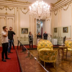 Tourists walk through Schönbrunn Palace with audio guides and take a look at the individual rooms. Red carpet, shining chandeliers, baroque furniture and golden decorations on the walls.