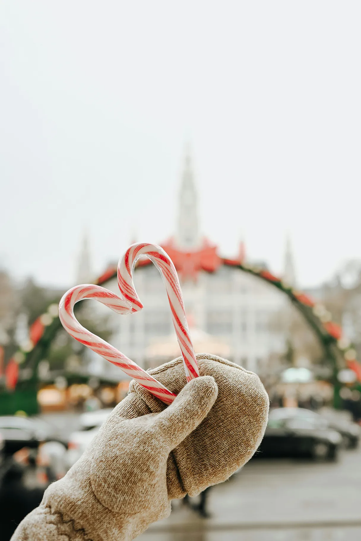 Two candy canes are held together to form a heart. The Christmas market on Vienna's Rathausplatz can be seen in the background. A huge swing arch with candles and Christmas decorations.