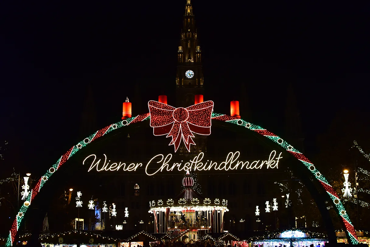 Vienna Christmas Market on Rathausplatz in Vienna. Huge candle arch illuminated with LED lights. In the background you can faintly see the town hall tower. It is dark and only the various lights from the Christmas market are shining.