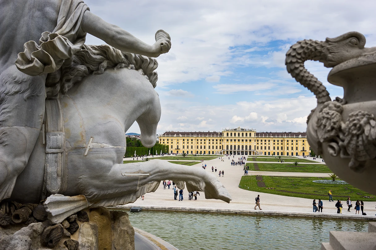 Blick auf das Schloss Schönbrunn, am Rand stehen weiße Skulpturen durch die man vorbei guckt