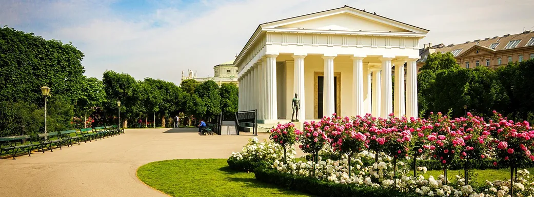 Griechischer Tempel im Volkgarten Wien. Ein sonniger Tag und die Rosenhochstämmchen blühen pink am rechten Rand.