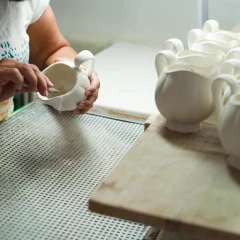 Augarten Porcelain Museum. An employee is working on the white porcelain blanks. In front of her is a board with many white porcelain cans.