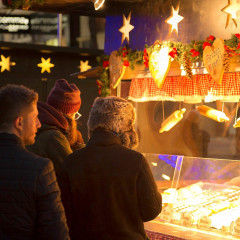 Weihnachtsmarkttour Eine Gruppe Touristen steht vor einem Weihnachtsmarktstand und schaut in die Auslage.