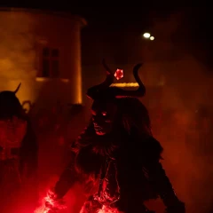 A Krampus figure stands in the fog. A red light shines up from below. A spooky atmosphere.